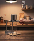 Minimalist Silver Finish Pour Over Coffee Dripper With Solid Metal Base, user handling the reusable brewer in a kitchen setting.
