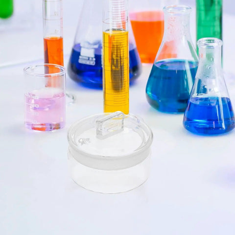 60x30 mm Graduated Glass Measuring Flask With Ground Glass Stopper surrounded by colorful lab liquids