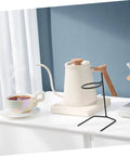 Pair Of Portable Coffee Dripper Holder And Filter Stand For Home Barista Rigs Or Weekend Warrior Campout Vibes Smooth Pour Station showing black metal stand beside a white kettle and cup.