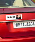 Rear view bumper sticker magnet, white with i brake for text and small portrait photo on red car.