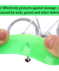 Close-up of Two Pack Green Bike Tire Liners being bent by hands, demonstrating puncture resistance with a bike wheel in the background.