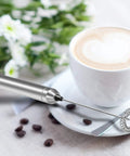 Milk Frother Handheld Electric Foamer Portable Mini Mixer Stainless Steel Body With Thick Whisk next to a cup of coffee