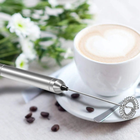 Milk Frother Handheld Electric Foamer Portable Mini Mixer Stainless Steel Body With Thick Whisk next to a cup of coffee