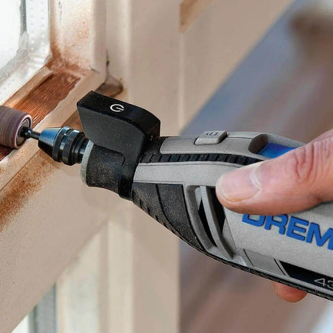 Side view of a Dremel rotary tool with 1/2-inch coarse sanding bands attached, sanding a wooden window frame.