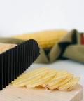 Potato crinkle cutter, black, close-up view slicing potatoes on a wooden cutting board