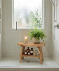 24 Inch Teak Shower Bench With Storage Shelf Waterproof Bathroom Seat For Adults And Seniors Spa Style Teak Wood Stool With Non Slip Feet Elegant Finish Supports Up To 300 Pounds placed in shower with plant and candle on top