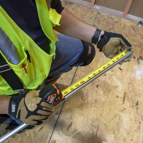 Worker using rugged 16 foot tape measure with double hook, nylon reinforced blade, measuring on construction site.