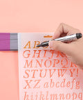 Hand using marker on stencil from Eight Pieces Personalized Pencil Name Plate Set With Blank Wooden Desk Signs, Marker Pen And English Letter Template, Custom Teacher Gift For Classroom Decor, Cute Pencil Shaped Name Tags For School And Party Supplies, including pencil shape and stencil for School and Party Supplies
