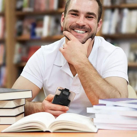 Man holding smartphone with upgraded Bluetooth barcode scanner with back clip in library setting surrounded by books.