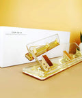 Clear Acrylic 3 Hole Punch For 10 Sheets With Four And A Quarter Inch Hole Spacing Gold Accents on desk with box and plant