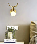 Brass Antlers Wall Sconce With E27 Socket above bedside table, showcasing modern design with soft lighting for cozy ambiance.
