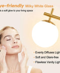 Next Level Three Light Bathroom Vanity Lights In Brushed Gold Finish With Milky White Glass Globe Shades Modern Wall Sconce Over Mirror illuminating a model's face.