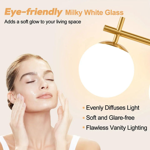 Next Level Three Light Bathroom Vanity Lights In Brushed Gold Finish With Milky White Glass Globe Shades Modern Wall Sconce Over Mirror illuminating a model's face.
