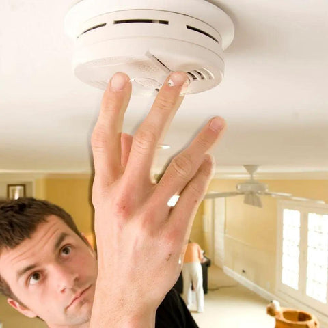 Man testing Hardwired Interconnectable Smoke Detectors With Battery Backup And Hush Button 120 Volt Wall Or Ceiling Mounted Fire Safety Alarms.
