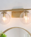 Gold Vanity Light 2-Light Fixture With Globe Clear Glass Shades For Bathroom, mounted above a mirror, modern design