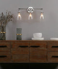 Three Light Industrial Wall Sconce With On Off Switch And Clear Glass Shade For A Cool Retro Vibe Vintage Antique Brass Vanity Lighting For Bathroom And Living Room Dimmable When Paired With A Compatible Dimmer Bell Shade Finish, installed above a wooden sideboard.