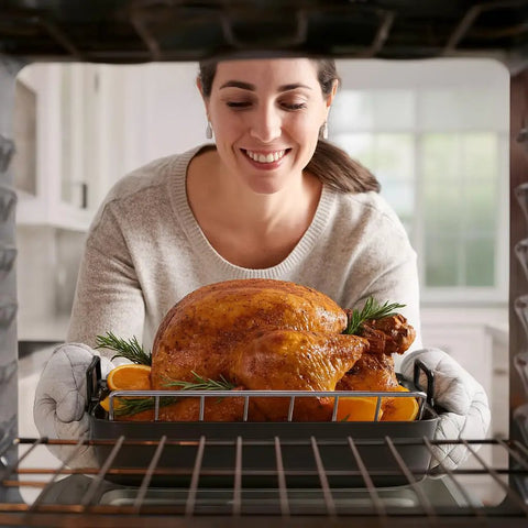 Person placing turkey in oven on V Shaped Roasting Rack For Even Cooking And Juicy Results Chrome Plated Steel Elevates Meat Poultry And Vegetables For Crisp Skin And Tender Interiors Dimensions 15.75 Inches By 10.25 Inches By 4 Inches