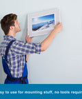 Person hanging a picture using Heavy Duty Double Sided Mounting Tape for Picture Hanging and Wall Art, no nails needed.