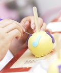 Hand using Six Piece Stainless Steel Cookie Scribe Tools And Sugar Stir Needles on yellow fondant for detailed decoration.