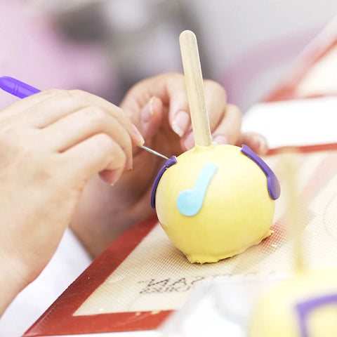 Hand using Six Piece Stainless Steel Cookie Scribe Tools And Sugar Stir Needles on yellow fondant for detailed decoration.