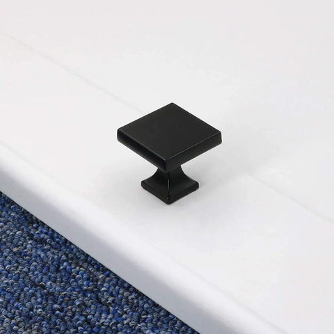 Black square cabinet knob on white surface, part of 10 Pack Black Cabinet Knobs For Dresser Drawers And Kitchen Cabinets Round 1.26 Inch Zinc Alloy Handles Sleek Matte Finish Dope Upgrade With Easy Install For Your Cabinets.