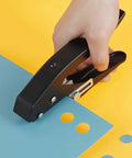 Hand using Heavy Duty 15 mm Round Hole Punch Tool For Paper, 20 Sheets Capacity, crafting precise circle holes on blue paper.