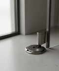 Solid Zinc Alloy Door Stopper With Suction Holder For Floor And Walls Holds Tight Against Wind To Keep Bedroom Office Quiet And Safe From Slams, positioned on a gray floor.