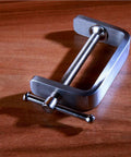 Angled view of stainless steel C-clamp with threaded screw and T-bar handle on wood