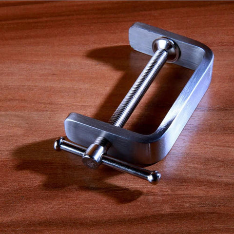 Angled view of stainless steel C-clamp with threaded screw and T-bar handle on wood