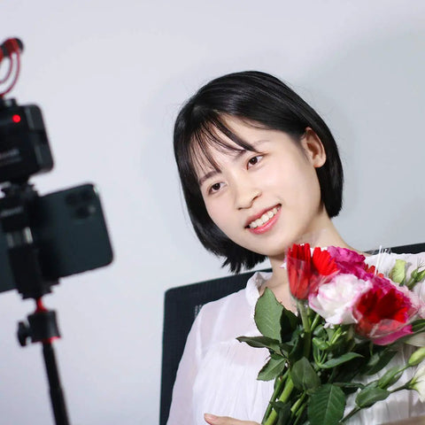 Woman holding flowers illuminated by VL49 2000mAh LED Video Light With 3 Cold Shoe Mounts for vlogging, with soft daylight lighting.