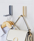Slick Foldable Wall Hooks With Adhesive Backing For Space Saving No Drill Setup To Hang Jackets Purses Hats Or Dog Leashes In Foyer Closet Easy Install Design Works As A Lifesaver To Keep Home Clutter Free Always Two Pack. Image shows gray and beige foldable hooks holding a purse and shirt.