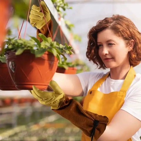 Woman wearing Rugged Leather Work Gloves For Men And Women Built Tough Cowhide Gardening Gloves Puncture And Cut Resistant With Elbow-Length Gauntlet For Thorny Pruning And Tough Yard Work while handling a plant pot in a garden.