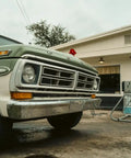 Vintage green and white truck in front of a retro gas station with American flags on a cloudy day.