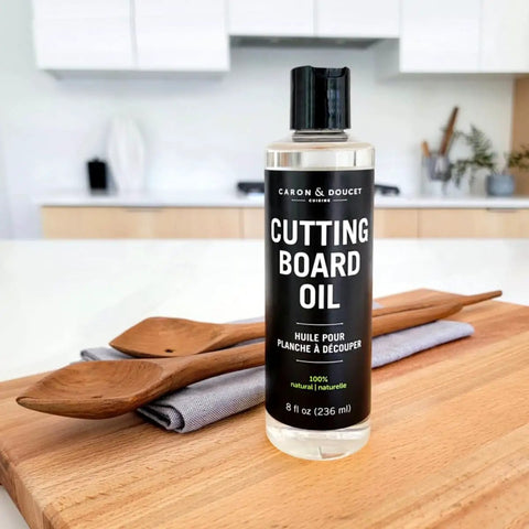 100 Percent Coconut Derived Cutting Board Oil For Wood And Bamboo Conditioning And Finishing Vegan Mineral Oil Free Non Toxic Sealant For Kitchen Boards No Mess 8 Oz bottle on kitchen counter next to wooden spoons and cloth folded on cutting board