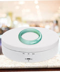 White Electric Rotating Display Stand For Jewelry Watches And Cosmetics Automatic Turntable Showcase With Stable Structure Energy Saving Design Perfect Gift Idea featuring a green ring on top.