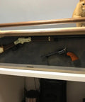 Wooden display case with vintage firearms and a cat peering over it.