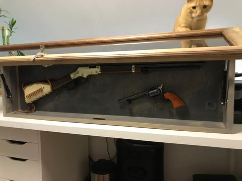 Wooden display case with vintage firearms and a cat peering over it.