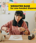 Woman using a black desktop tape dispenser, black polystyrene, weighted base, one-hand dispensing, refillable 1-in core