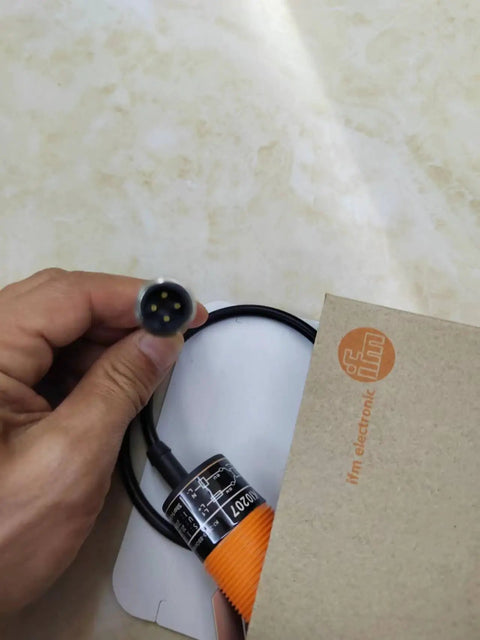 Hand holding KI0207 Capacitive Proximity Sensor Switch For Automation and Robotics Control with visible connector plug