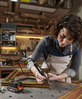 A woman using the Top Tier Cordless Pen Engraver And Digital Soldering Iron Kit With Sweet 20V Battery on a wood frame.