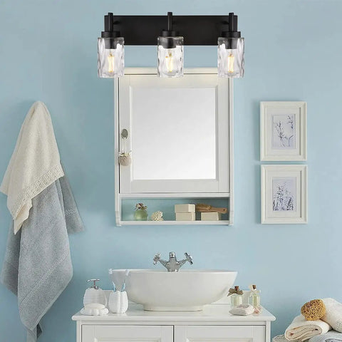 Three Light Modern Vanity Wall Sconce In Black With Hammered Glass Shades above bathroom mirror cabinet in modern setting.