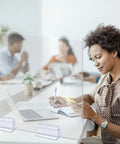 Woman using phone at a desk with Six Pack Heavy Duty Self Adhesive Sneeze Guard Holders for quarter inch acrylic sheets.
