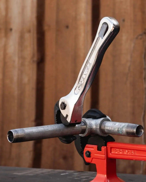 Top Shelf Nine Inch Compact Pipe Wrench Built Like A Tank For Killer Grip On Half To One Inch Fittings, chrome plated, gripping metal pipes in a vise.