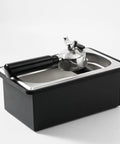 Built Like A Tank Stainless Steel Knock Box With Removable Interior Grounds Bin For Espresso Setups and Home Baristas Made For Busy Coffee Shops Without The Headache Featuring Durable Metal Construction, angled view with handle.