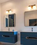 Gold Two Light Wall Sconce With Brass Finish And Milky White Glass Globe above bathroom mirrors in contemporary setting.