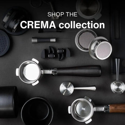 Assorted coffee tools including portafilters, tamper, and scoops from the CREMA collection on a dark surface.