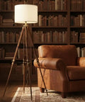 Vintage Tripod Floor Lamp With Nautical Vibe And Dope Rustic Industrial Finish In Steel Aluminum And Brown Wood Antique Brass Accent Shade Not Included next to leather armchair in library.