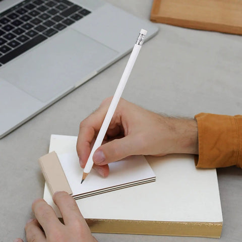 Person using a white carpenter pencil with eraser from Ten Pack White Carpenter Pencils With Eraser For Construction And Woodworking, Solid Graphite Marking Pencils For Builders, Engineering Drawings, Office And School Use, Durable Bulk Pack For Pros And DIYers to write on small notepad near laptop.