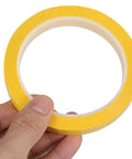 Close-up of a hand holding a roll of Four Pack Yellow Heat Resistant Paper Tape Featuring A Dang Tough Hold That Takes The Heat Without Breaking A Sweat Ideal For Neat Cable Organizing Bold Project Labeling And Reliable Everyday Fixes In Offices Or Workshops Everywhere.