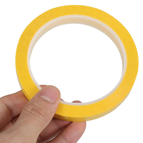 Close-up of a hand holding a roll of Four Pack Yellow Heat Resistant Paper Tape Featuring A Dang Tough Hold That Takes The Heat Without Breaking A Sweat Ideal For Neat Cable Organizing Bold Project Labeling And Reliable Everyday Fixes In Offices Or Workshops Everywhere.
